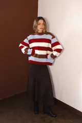 Buzo tejido de punto con diseño de rayas horizontales anchas en colores marrón, blanco, rojo y celeste. Presenta cuello redondo, corte holgado y mangas largas con puños acanalados.