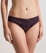 Bombacha modelo bikini confeccionada en encaje con diseño floral, presenta bordes festoneados y una pequeña medalla metálica decorativa en el centro de la cintura. Cuenta con forro interior de algodón.