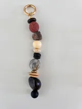 Colgante decorativo para bolso o llavero, compuesto por una cadena metálica con un conjunto de cuentas de diferentes formas, colores y texturas, incluyendo piedras naturales y cuentas de madera.