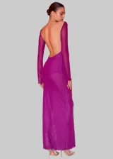 Vestido largo de tul transparente color magenta, con cuello redondo, mangas largas y espalda descubierta. Presenta un tajo lateral profundo en la falda.