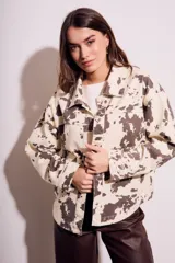 Campera de algodón color crema con estampado de manchas marrones tipo vaca, corte al cuerpo, con cuello clásico, cierre frontal con botones y bolsillos de parche en el pecho.