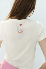 Camiseta blanca de algodón con cuello redondo, manga corta y calce regular. Presenta un estampado frontal ilustrado con conejos, corazones, estrellas y el texto "Kindness for every kind".