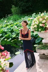 Vestido largo azul marino con tirantes anchos, escote en V y detalles de volantes rojos en el busto y la cintura. La falda es ajustada hasta la rodilla y luego se abre en una capa de tela transparente hasta el tobillo.