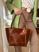 Cartera tipo shopper de cuero genuino color marrón con estampado texturado tipo cocodrilo. Presenta detalles de costuras y tiras trenzadas artesanales en los bordes y en las asas de hombro.