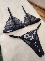 Conjunto de lencería compuesto por un bralette triangular y una bombacha tipo tanga, confeccionados en encaje negro con detalles florales en hilo plateado.