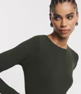 Suéter de punto color rosado, con cuello barco, mangas largas y puños con botones decorativos. El dobladillo también es acanalado.