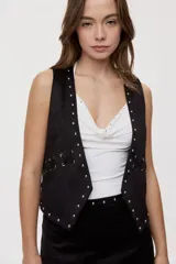 Chaleco de efecto gamuzado color negro, abierto con escote en V, detalles de tachas metálicas en los bordes y cordones entrelazados en los laterales.
