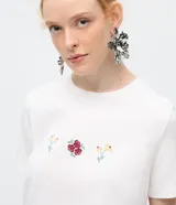 Remera de algodón color blanco, de corte clásico con cuello redondo y manga corta. Presenta un delicado bordado de tres pequeños íconos florales en el centro del pecho.