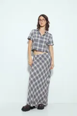 Camisa de manga corta con cuello camisero y botones frontales. Presenta un estampado de cuadros escoceses en tonos marrón oscuro y blanco/beige, con un calce entallado.