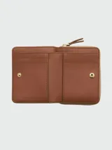 Billetera compacta con cierre de cremallera, color rosado pálido, con textura de cuero granulado. Presenta el texto "THE WALLET MARC JACOBS" estampado en el frente.