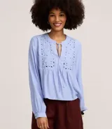 Blusa tipo bata de color celeste con mangas largas y cuello mao con lazo. Presenta detalles de bordado floral calado tipo laise en el frente y cierre parcial con botones.