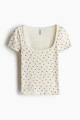 Remera corta de manga corta en punto acanalado, de color beige con estampado floreado pequeño, escote cuadrado y ribete de picot.
