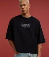 Remera negra de algodón con corte oversized, cuello redondo, mangas cortas y estampa tribal blanca en el pecho.