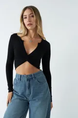 Top de manga larga en tejido rib negro, con escote en V profundo y detalle de nudo frontal que genera un efecto fruncido.