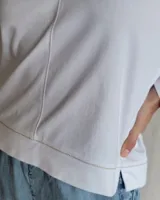 Remera de algodón color blanco, con escote en V y detalle de pespuntes decorativos en color beige. Presenta mangas largas y un corte recto con aberturas laterales en el ruedo.