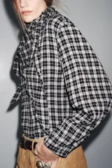 Camisa de manga larga con estampado a cuadros en blanco y negro. Presenta un cuello redondo y un pañuelo multiposición que cae en un drapeado asimétrico sobre el frente.