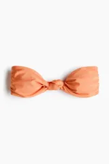 Top de bikini strapless color salmón con un nudo decorativo en el centro, copas con relleno extraíble y varillas laterales.