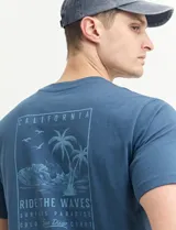 Remera azul con estampa en la espalda de palmeras, olas y texto "California, Ride the Waves, Surfers Paradise, Gold San Diego Coast".