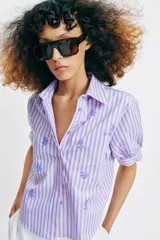 Camisa de cuello solapa y mangas cortas abullonadas, con diseño de rayas verticales en tonos rosados y celestes, decorada con lentejuelas bordadas.