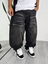 Pantalón de jean corte baggy, color negro con efecto lavado y estampado de rayas horizontales desgastadas en los muslos. Presenta costuras en contraste y diseño holgado.