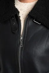 Campera tipo gamulán de cuero sintético negro con interior y detalles de cuello y puños en corderito negro. Presenta cierre frontal y diseño oversize.