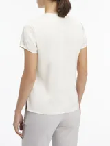 Blusa blanca de satén con cuello redondo con abertura en forma de V y mangas cortas.