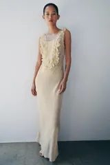 Vestido largo color beige de viscosa, con escote cuadrado, tirantes anchos, detalles drapeados, volantes y aplicaciones de encaje a contraste en el pecho. Cuenta con cierre trasero de botones.
