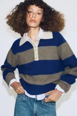 Jersey de punto a rayas horizontales azules y grises, con cuello tipo polo en color beige y cierre frontal con botones.
