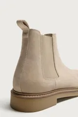 Bota Chelsea de hombre en color beige, confeccionada en piel con acabado serraje. Cuenta con elásticos laterales, trabilla trasera para facilitar el calce y suela plana con ligero tacón.