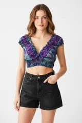 Top corto ajustado al cuerpo, con escote profundo en V con volados, mangas cortas abullonadas y elástico fruncido en la base. Presenta un estampado floral en tonos morados, azules y verdes.