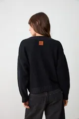 Sweater de punto texturizado color negro, con cuello en V acanalado, mangas largas y corte holgado con terminaciones en puños y ruedo acanalados.