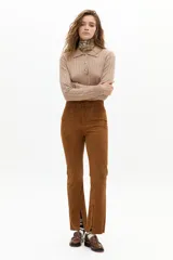 Pantalón de corte recto confeccionado en gamuza de cabra color marrón tostado. Presenta tiro medio con elástico interno en la cintura, cierre frontal con gancho metálico y tajos en el ruedo.
