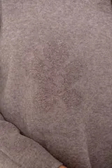 Buzo de punto color visón con cuello alto, manga larga y diseño holgado. Presenta un bordado floral en relieve al tono en la parte frontal.