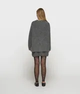 Sweater de punto oversize color gris, confeccionado en una mezcla de lana de alpaca con textura suave y peluda. Presenta cuello en V, mangas largas con hombros caídos y ribetes de canalé. Incluye una etiqueta decorativa en el puño de la manga izquierda.