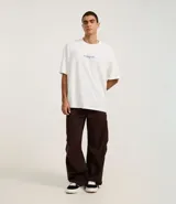 Remera de algodón blanca, corte oversized, con estampa gráfica en la espalda que incluye un teléfono antiguo, un CD, una cámara fotográfica, auriculares y un reproductor de CD portátil, junto al texto "Analog Life - NO EDITS -".