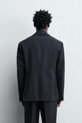Blazer de corte regular confeccionado en tejido de lana italiana. Presenta cuello con solapas de muesca, cierre frontal de un botón, bolsillos laterales con solapa y bolsillo de vivo en el pecho. Incluye aberturas en la espalda y forro interior.
