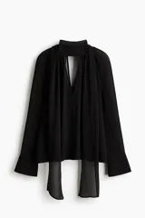 Blusa oversized negra de tejido transparente, con cuello fular, escote profundo y mangas largas con puños anchos.