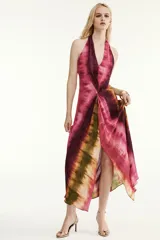Vestido midi de cuello halter y escote en V, con diseño tie-dye en tonos fucsia, borgoña y verde. Presenta un nudo decorativo en el delantero, espalda descubierta y abertura frontal en el bajo.