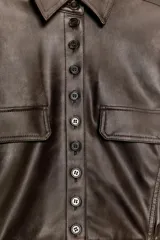 Cazadora de efecto piel con cuello solapa, manga larga y cierre frontal con botones. Presenta falsos bolsillos con solapa en el delantero y bajo con acabado peplum.
