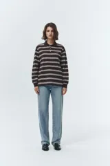 Remera tipo polo de manga larga, color marrón oscuro con rayas horizontales blancas y finas. Posee cuello polo y tapeta con botones.