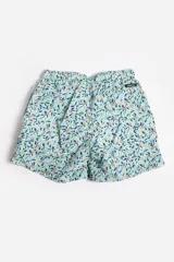 Short de baño celeste con estampado de hojas pequeñas en tonos verdes y blancos. Cuenta con cintura elástica con cordón ajustable, bolsillos laterales y un parche circular con logo en la parte inferior.