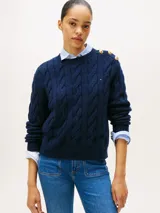 Sweater de punto con diseño de trenzas, cuello redondo y detalle de botones dorados en el hombro. Presenta terminaciones acanaladas en puños y dobladillo, con logo bordado en el pecho.