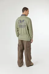 Remera tipo polo de manga larga en color blanco, con cuello en contraste color azul marino. Presenta un pequeño logo cuadrado con una X en el pecho y detalles de texto impreso en el lado derecho.