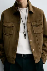 Cazadora de hombre de corte regular fit, color marrón oscuro, confeccionada en tejido efecto ante. Presenta cuello solapa, manga larga con puño abotonado, dos bolsillos de plastrón con solapa en el pecho y bolsillos laterales en la costura de la cadera. Cierre frontal con botones a presión.