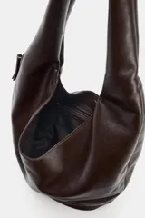 Bolso de hombro tipo saca en formato maxi, confeccionado en material sintético negro. Presenta un diseño holgado con asa integrada, cierre imantado en el compartimento principal, bolsillo lateral con cremallera y detalle de tirador.