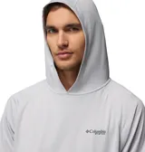 Remera de manga larga con capucha Columbia PFG, confeccionada en tejido técnico transpirable de secado rápido con tecnología Omni-Wick y protección solar Omni-Shade UPF 50. Presenta un diseño liso en color gris claro con el logo de la marca estampado en el pecho.