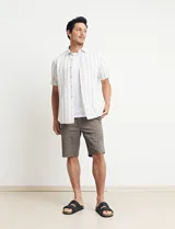 Camisa de manga corta a rayas verticales color natural y celeste, con cuello clásico, cierre frontal con botones de madera y bolsillo de parche en el pecho.