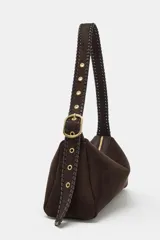 Bolso de hombro de diseño estructurado en color marrón, confeccionado en gamuza. Presenta un asa larga ajustable con detalle de trenzado y hebilla metálica dorada. Cuenta con cierre de cremallera con doble tirador y bolsillo interior.