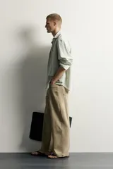 Pantalón relaxed fit de color beige, confeccionado en tejido con mezcla de algodón y lino, con diseño de cinco bolsillos, efecto lavado y cierre frontal con cremallera y botón.