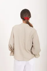Blusa de diseño cuadrillé en tonos beige y verde claro, de corte amplio y mangas largas abullonadas con puños elastizados con volados. Cuenta con cuello mao y una abertura frontal parcial con botones.